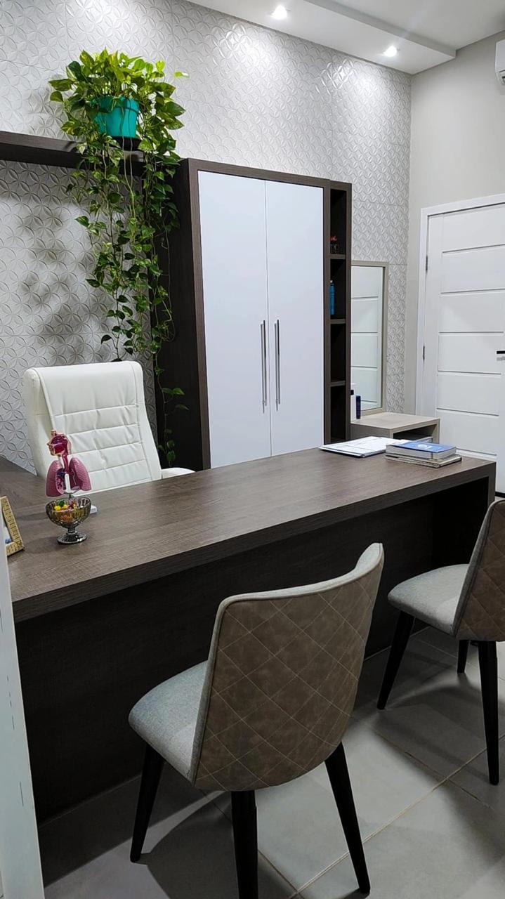 Consultório com mesa, cadeiras e armários brancos